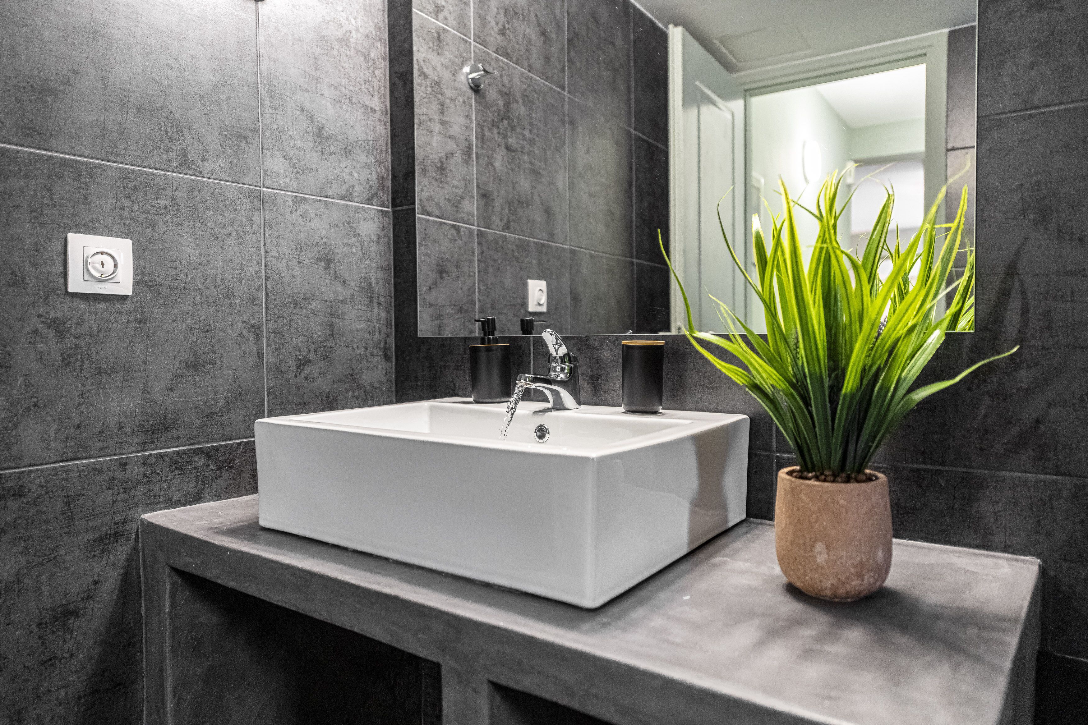 Uma casa de banho moderna com uma pia retangular, um espelho e uma planta em vaso.