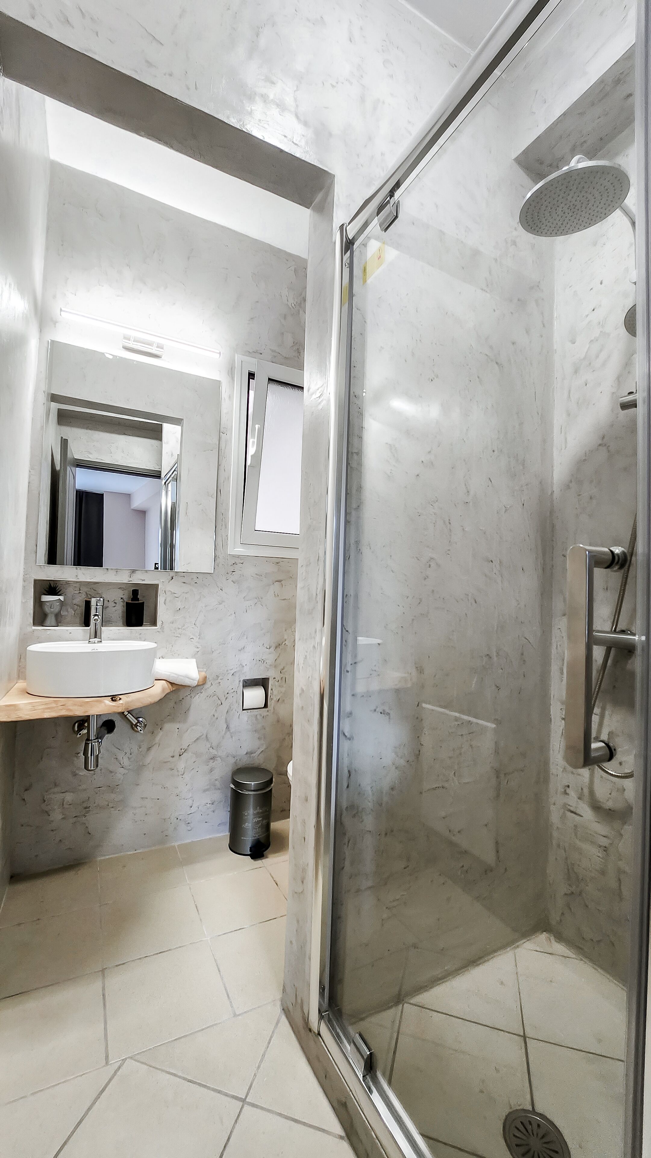 A modern bathroom with a glass-enclosed shower, a sink with a mirror above it, and a trash bin.