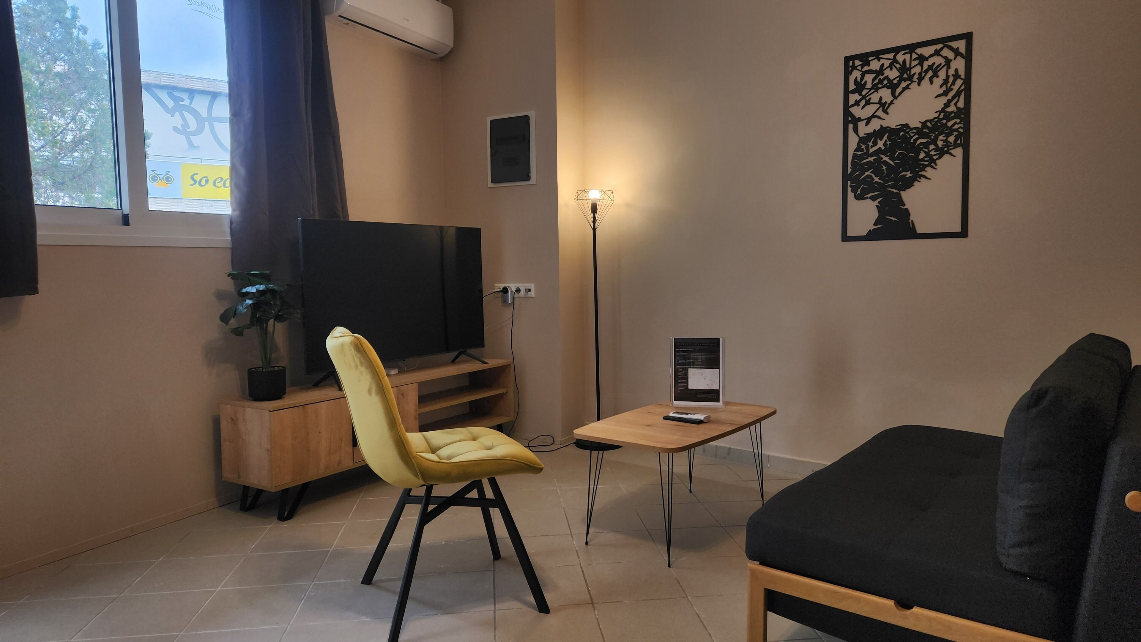 Una sala de estar con un sofá, una butaca amarilla, un televisor, una mesita y una lámpara de pie.