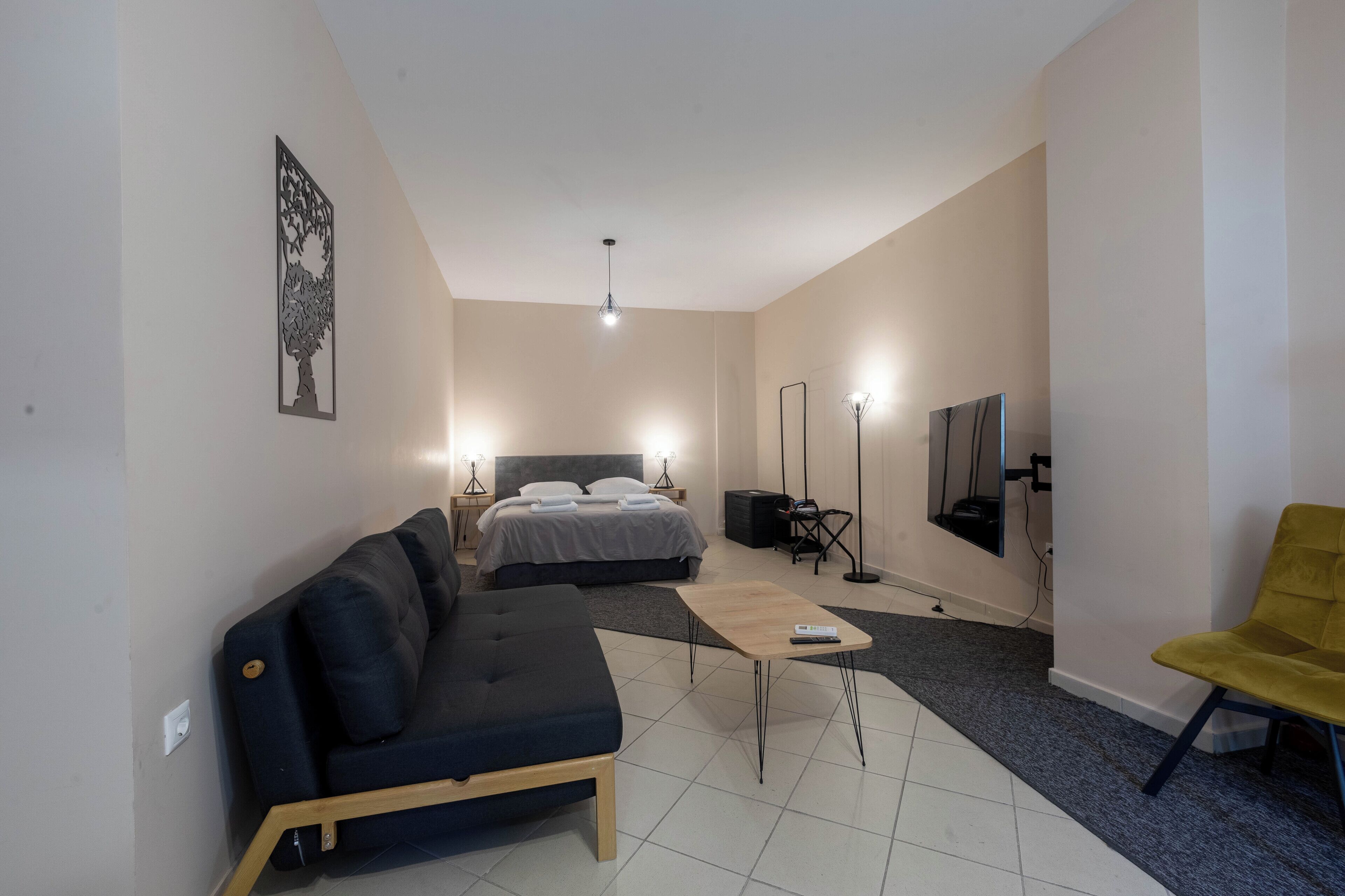 A modern hotel room with a bed, a sofa, a coffee table, a TV, and a chair.