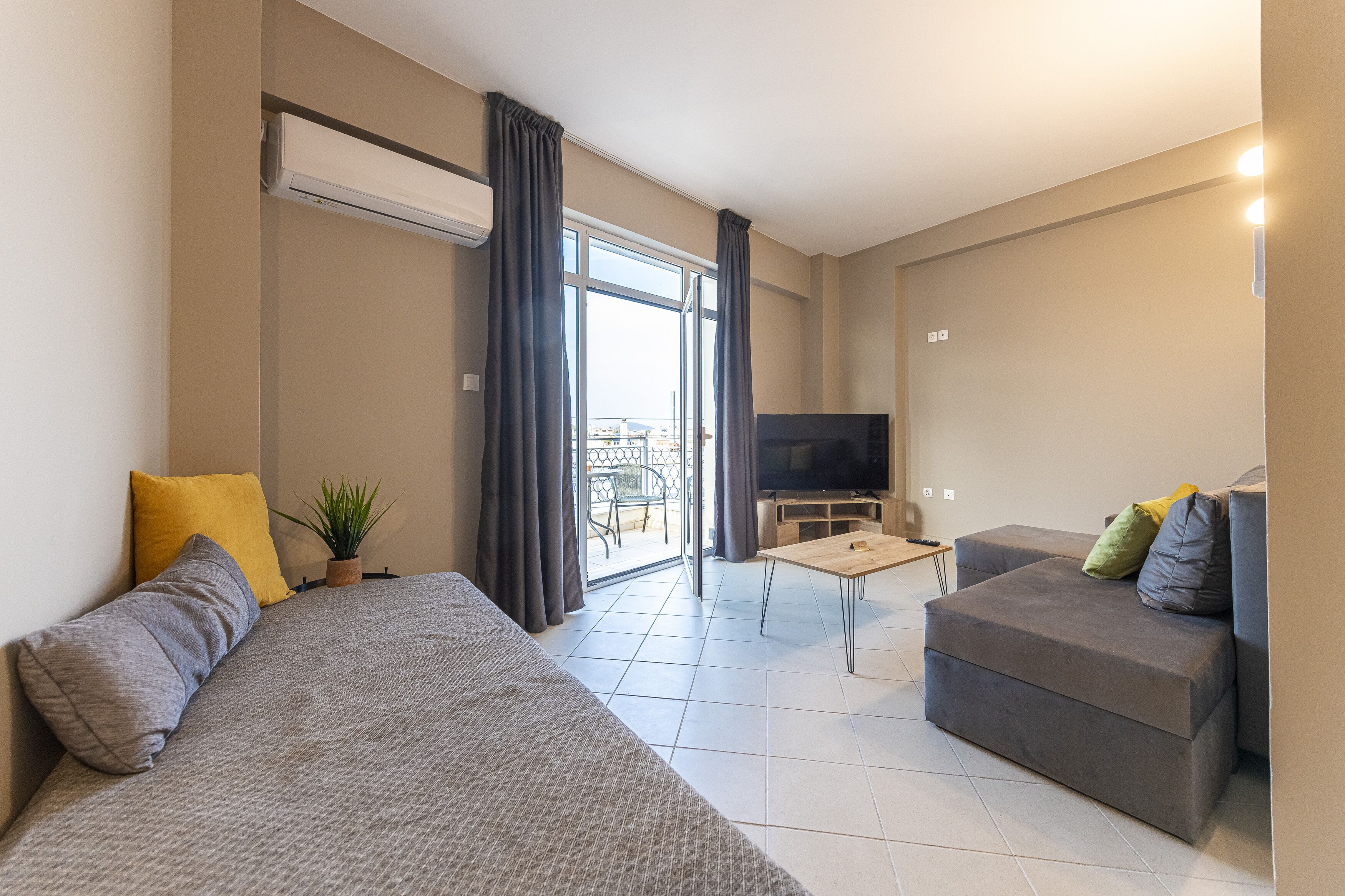 A modern living room with a sofa, a smaller couch, a TV, and a sliding glass door leading to an outdoor area.