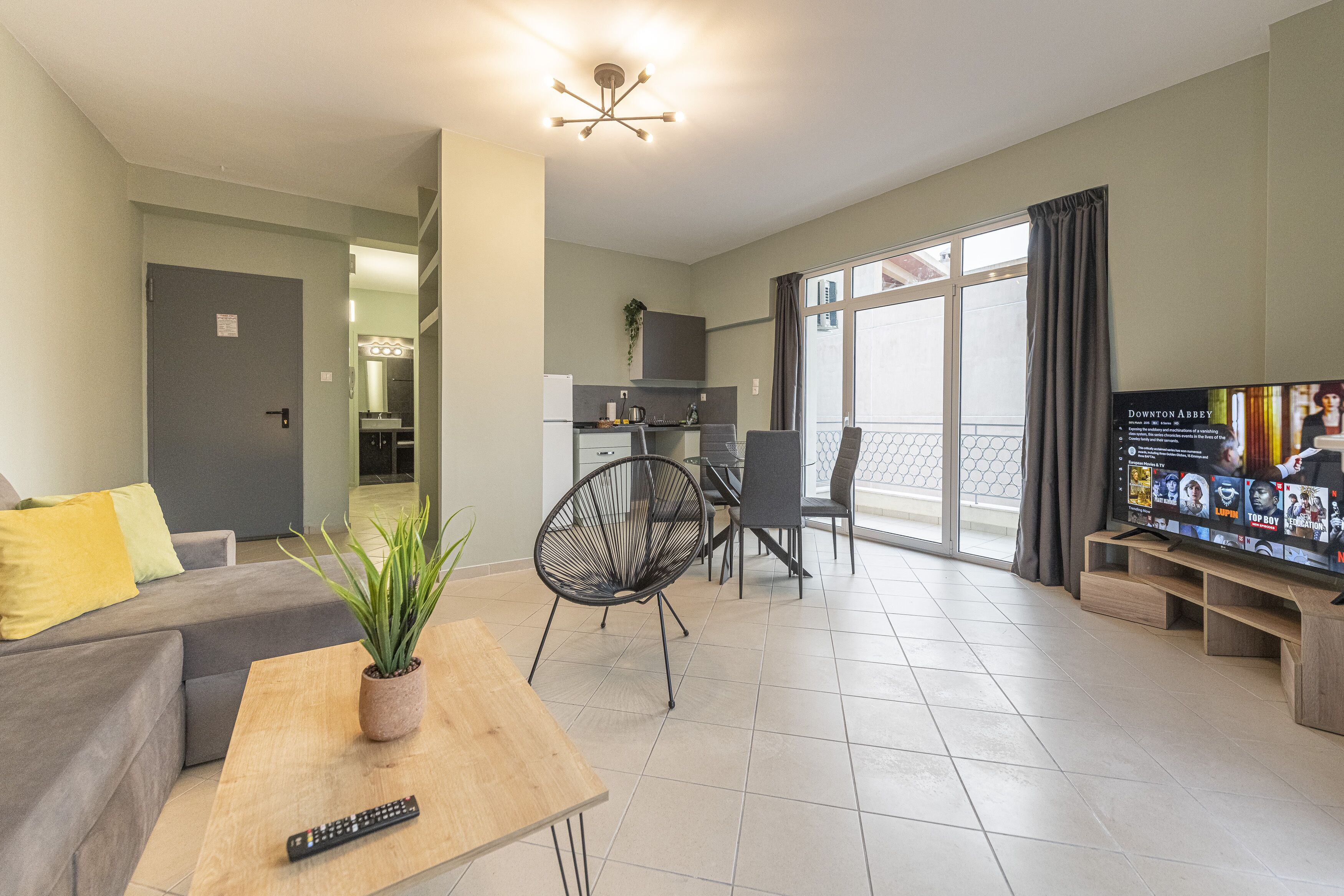 A modern living room with a sofa, a coffee table with a plant, a TV, and a dining area with chairs and a table.