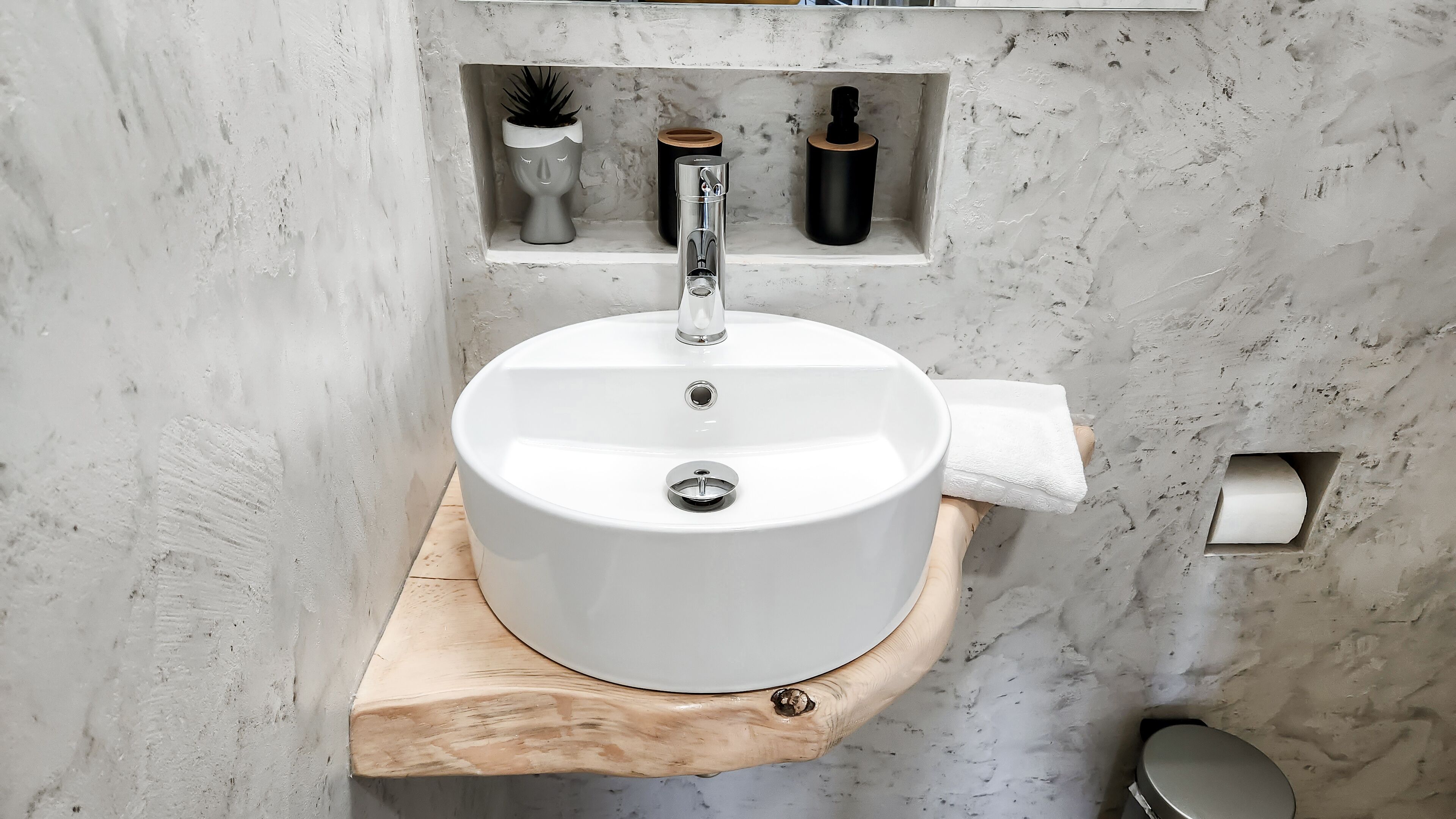 Une salle de bain avec un lavabo blanc posé sur une étagère en bois, une serviette et une petite étagère contenant des articles de toilette.