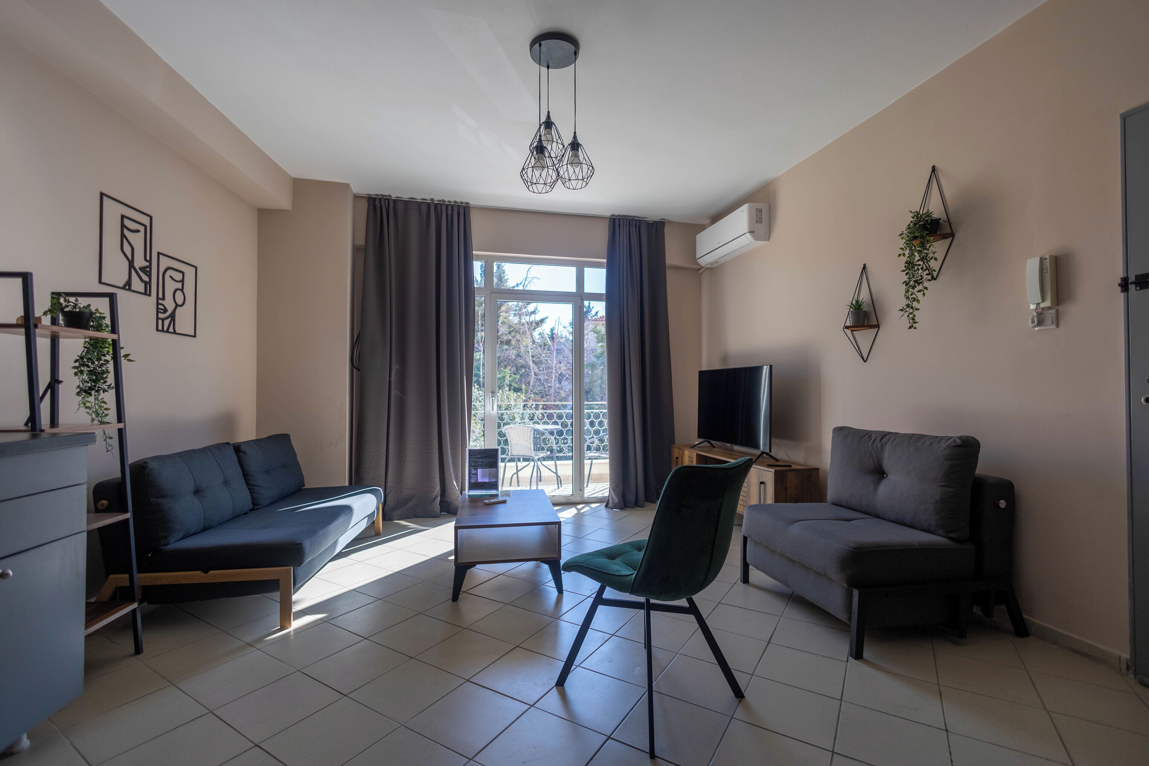 Uma sala de estar moderna com sofá, poltrona e televisão. Há uma janela com cortinas, uma luminária no teto e decoração na parede.