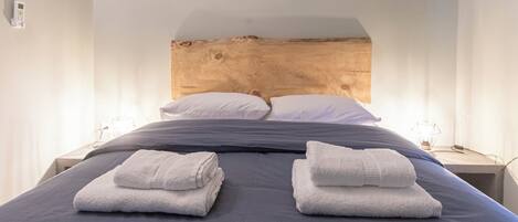 A neatly made bed with two folded towels, a wooden headboard, and bedside lamps.