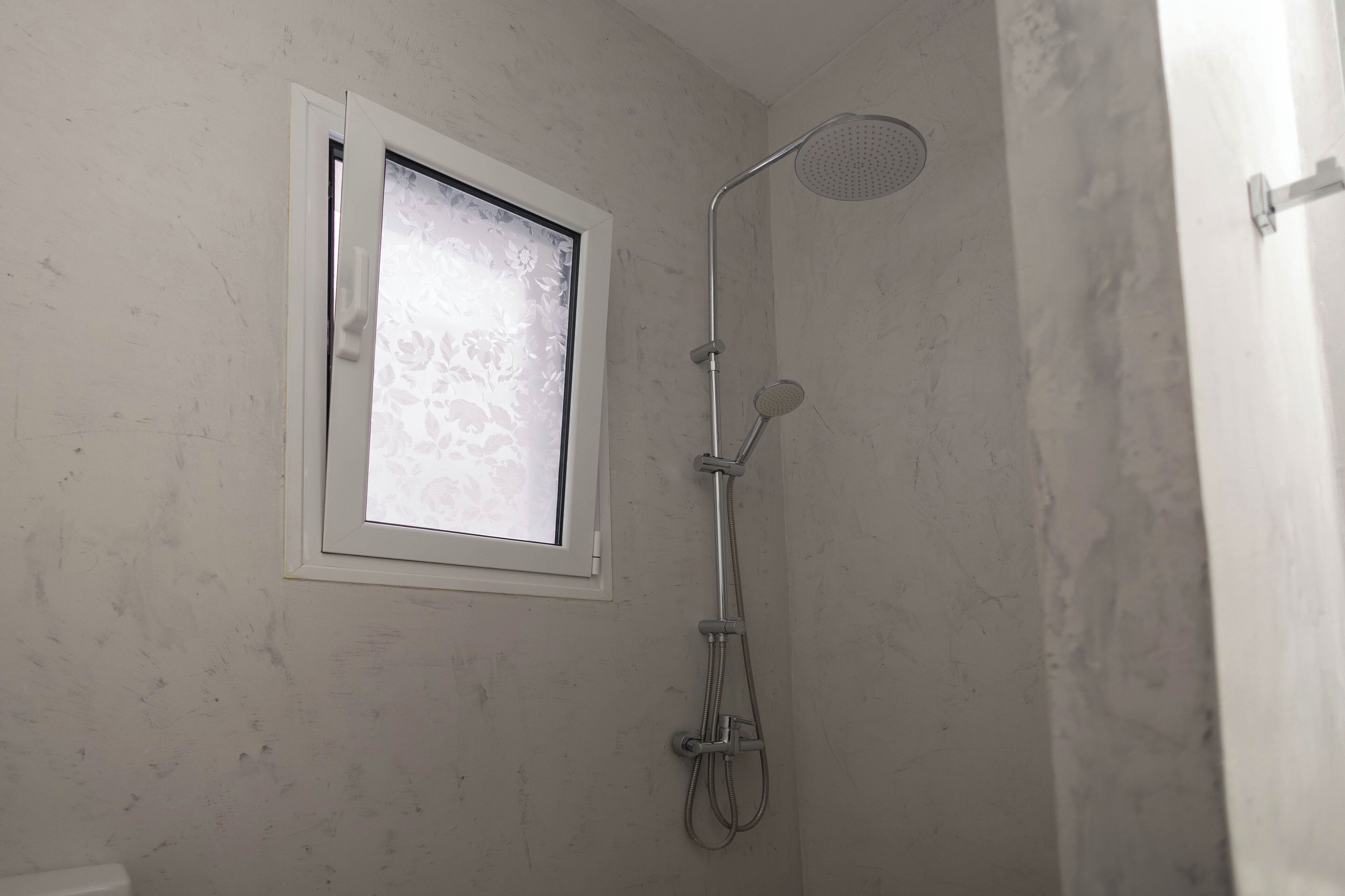 A bathroom with a shower, a window with frosted glass, and a white door.