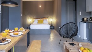 Een moderne hotelkamer met een groot bed, bedlampen, een houten ontbijtbalk en een kitchenette.