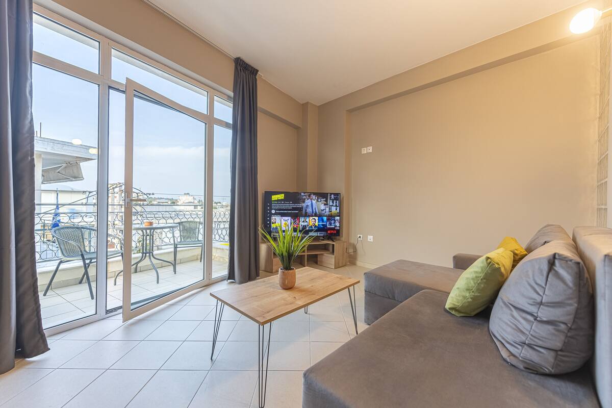 Un salon moderne doté d’un grand téléviseur, d’un canapé, d’une table basse et d’un balcon aménagé avec du mobilier d’extérieur.
