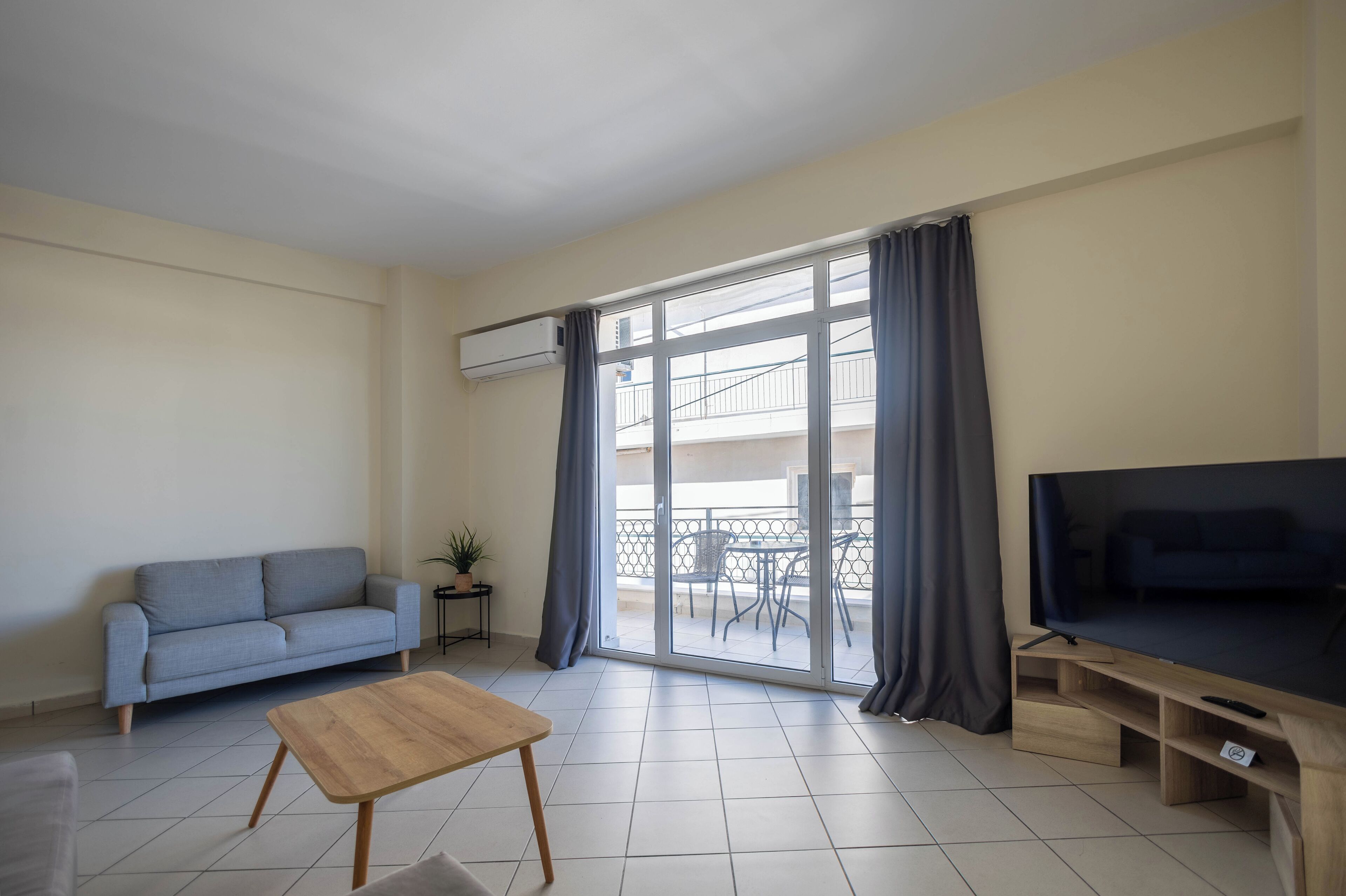 A living room with a sofa, a coffee table, a TV, and a sliding glass door leading to a balcony.