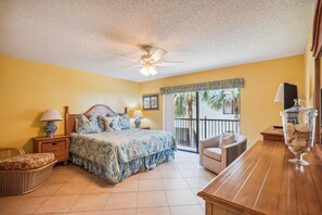 A bedroom with a bed, bedside tables, a chair, a balcony with a view, and a ceiling fan.