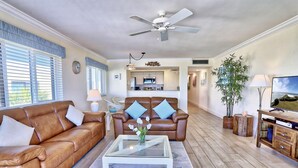 A living room with a brown leather sofa, a glass coffee table, and a television on a wooden stand. - Land's End 7-406 Beach Front - Premier (Treasure Island)