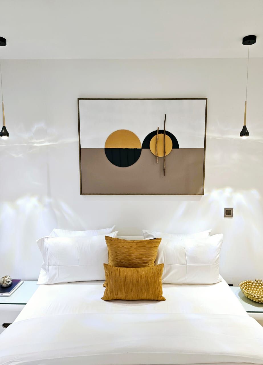 A bedroom with a bed, pillows, a wall-mounted abstract artwork, and pendant lighting.