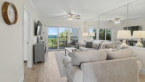 Ein Wohnzimmer mit Sofa, Fernseher, Deckenventilator und einem Balkon mit Blick.