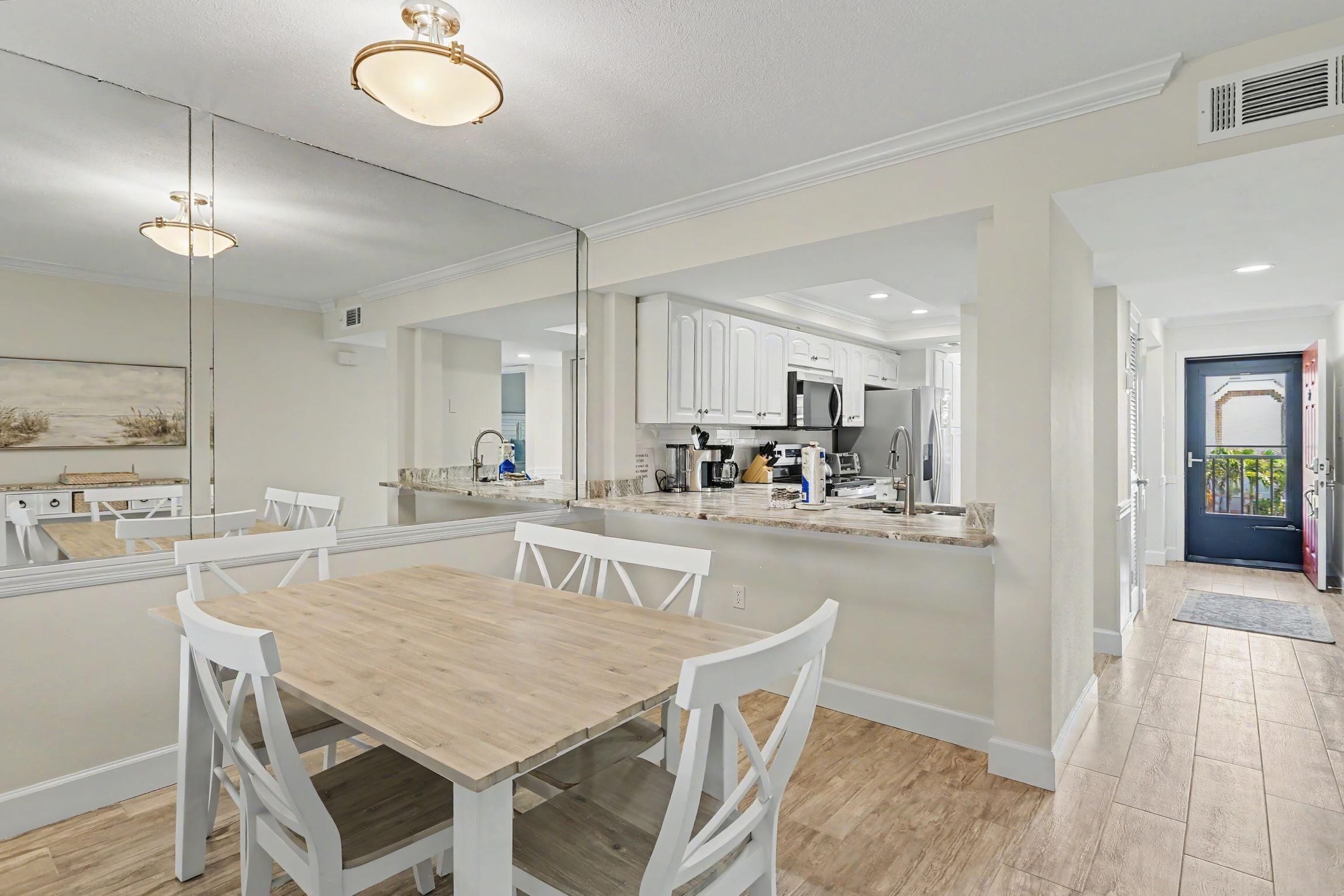 Una cocina moderna con armarios blancos, una mesa de comedor de madera y un espejo grande.