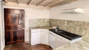 Eine kleine Küche mit Holztür, weißen Schränken, einer schwarzen Arbeitsplatte und einer gefliesten Spritzschutzwand.