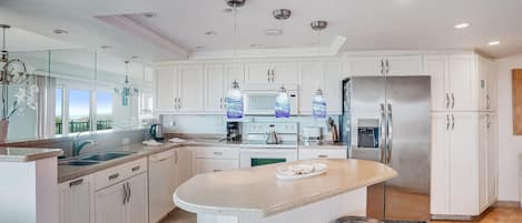 A modern kitchen with white cabinets, a stainless steel refrigerator, and a central island with stools.