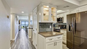 A modern kitchen with white cabinetry, a stainless steel refrigerator, and a microwave. - Land's End 9-304 Beach Front - Premier (Treasure Island)