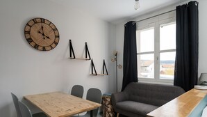 A modern living room with a wooden table, grey chairs, a grey sofa, a wooden clock, and a window with curtains. - Pretty ski nest in the city center (Gérardmer)