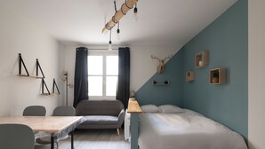 A modern room with a bed, a table with chairs, a window with curtains, and wall-mounted shelves. - Pretty ski nest in the city center (Gérardmer)