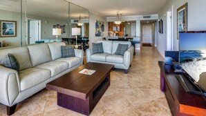 A spacious living room with a large sofa, a coffee table, and a TV. There is a kitchen in the background with a dining area. - Land's End 9-404 Beach Front - Premier (Treasure Island)