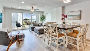 Un salon moderne avec un coin repas, de grandes fenêtres et un ventilateur de plafond.