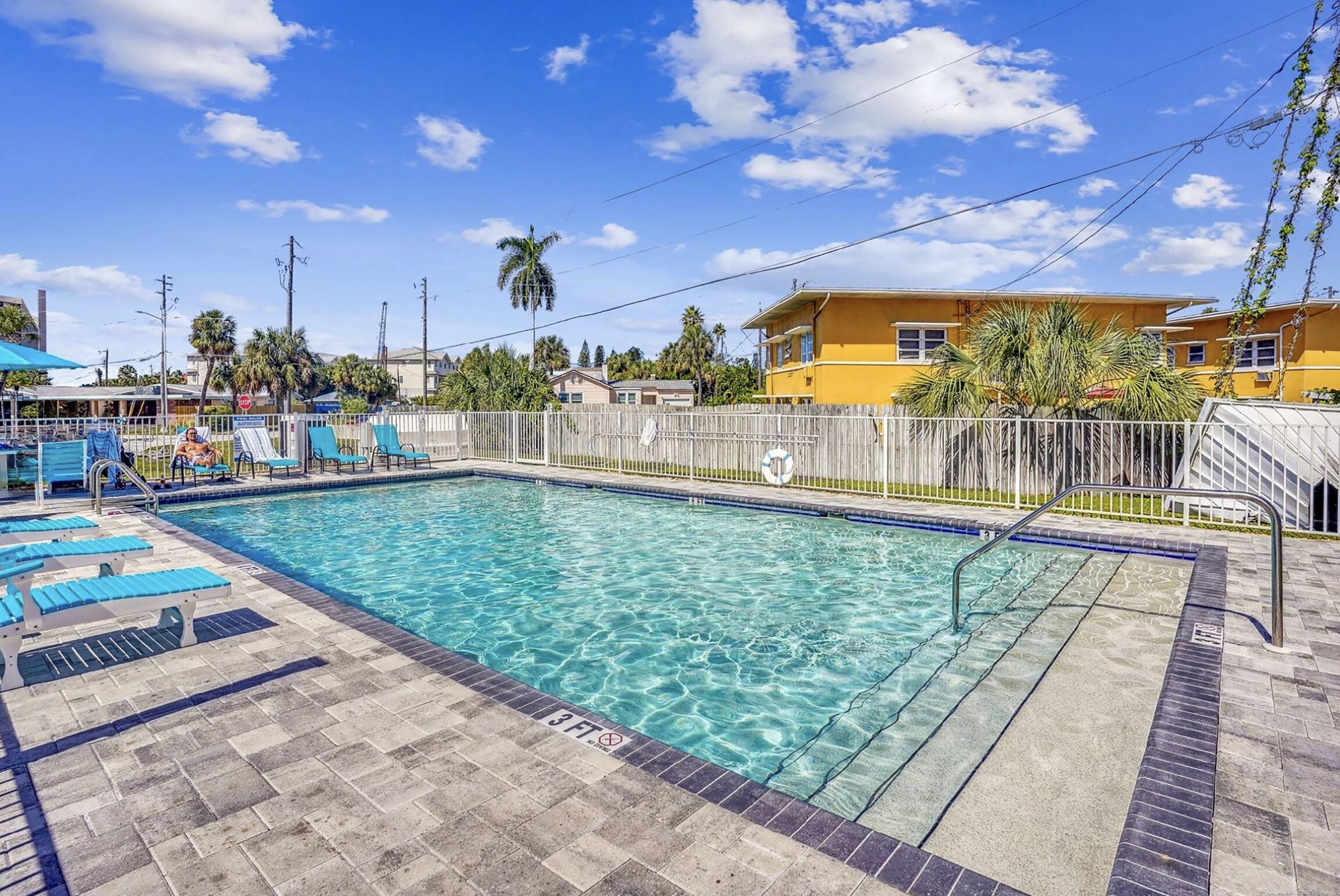 A swimming pool with clear water, surrounded by lounge chairs and a fenced area.