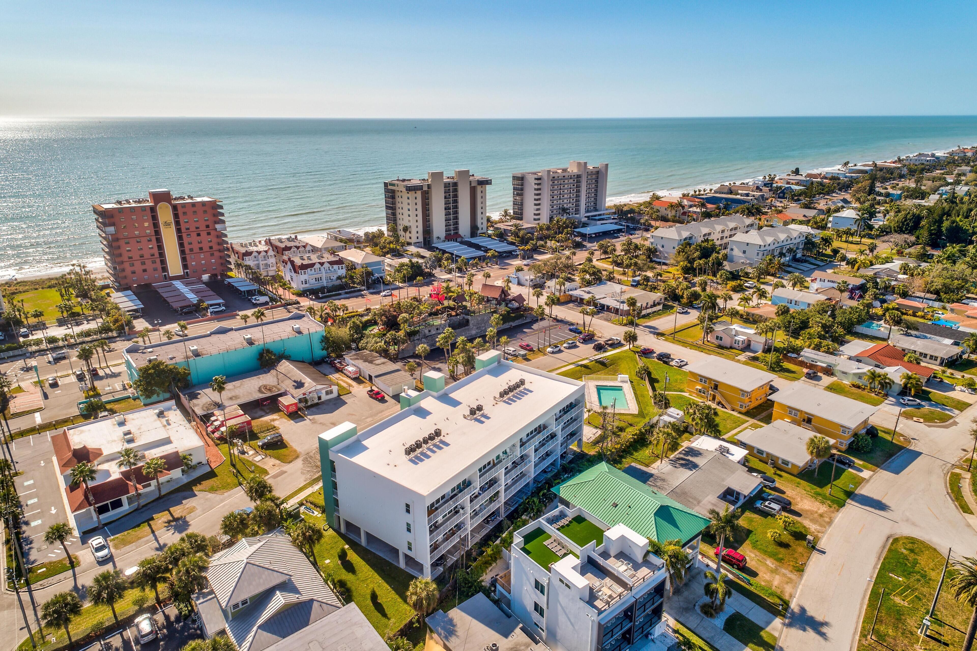 An aerial view of a coastal town with beachfront hotels, a large parking lot, and residential buildings.
