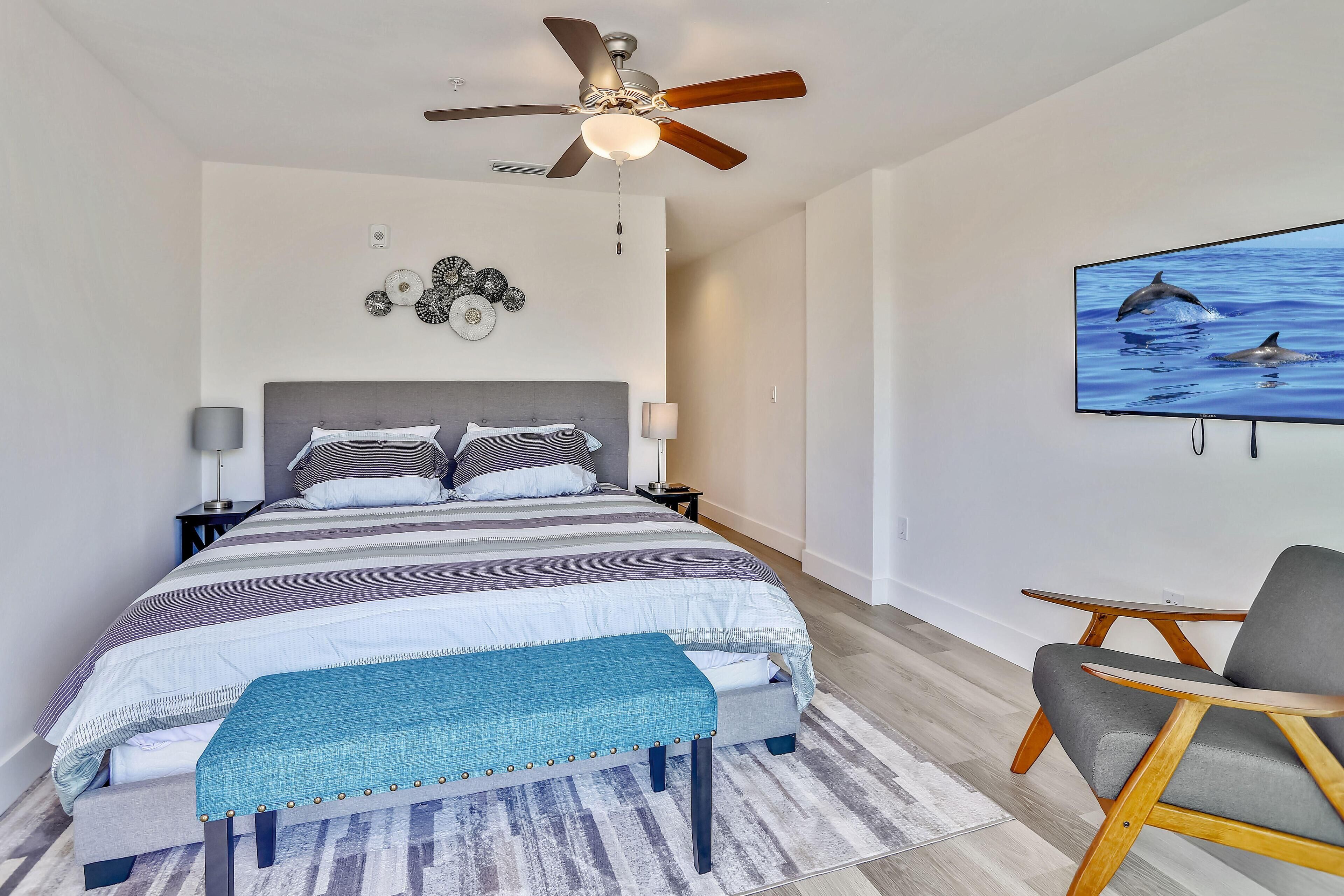 A bedroom with a bed, a ceiling fan, a wall-mounted TV, and a bedside table.