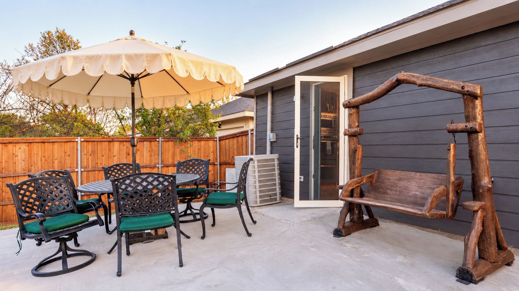 An outdoor patio with a wooden swing, a table with chairs, and a large umbrella.