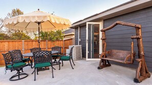 An outdoor patio with a wooden swing, a table with chairs, and a large umbrella.