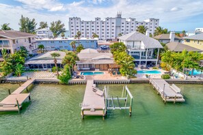A waterfront property with multiple swimming pools, a dock, and a view of a tall building in the background.
