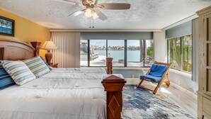 A bedroom with a bed, a ceiling fan, a view of the outdoors, and a chair by the window. - Manatee Home - Water Front Pool Home (Treasure Island)