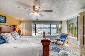 A bedroom with a bed, a ceiling fan, a view of the outdoors, and a chair by the window.