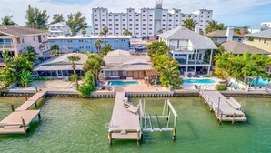 A waterfront property with multiple swimming pools, a dock, and a view of a tall building in the background. - Manatee Home - Water Front Pool Home (Treasure Island)