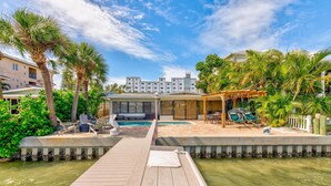 A waterfront property with a wooden dock, a pool area with lounge chairs, and a building with a covered patio. - Manatee Home - Water Front Pool Home (Treasure Island)