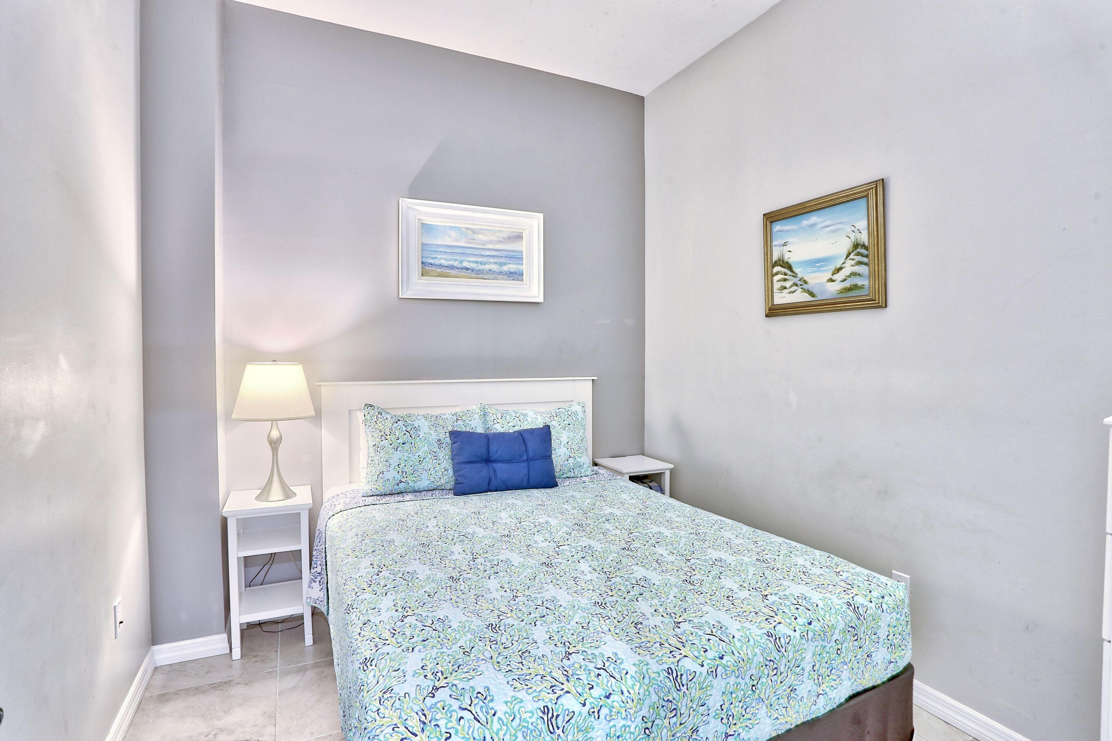 A bedroom with a bed, a nightstand, a lamp, and two framed pictures on the wall.