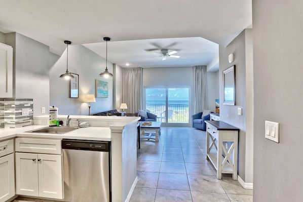 A modern kitchen with a dishwasher, a dining area with a table and chairs, and a view of the ocean through large windows.