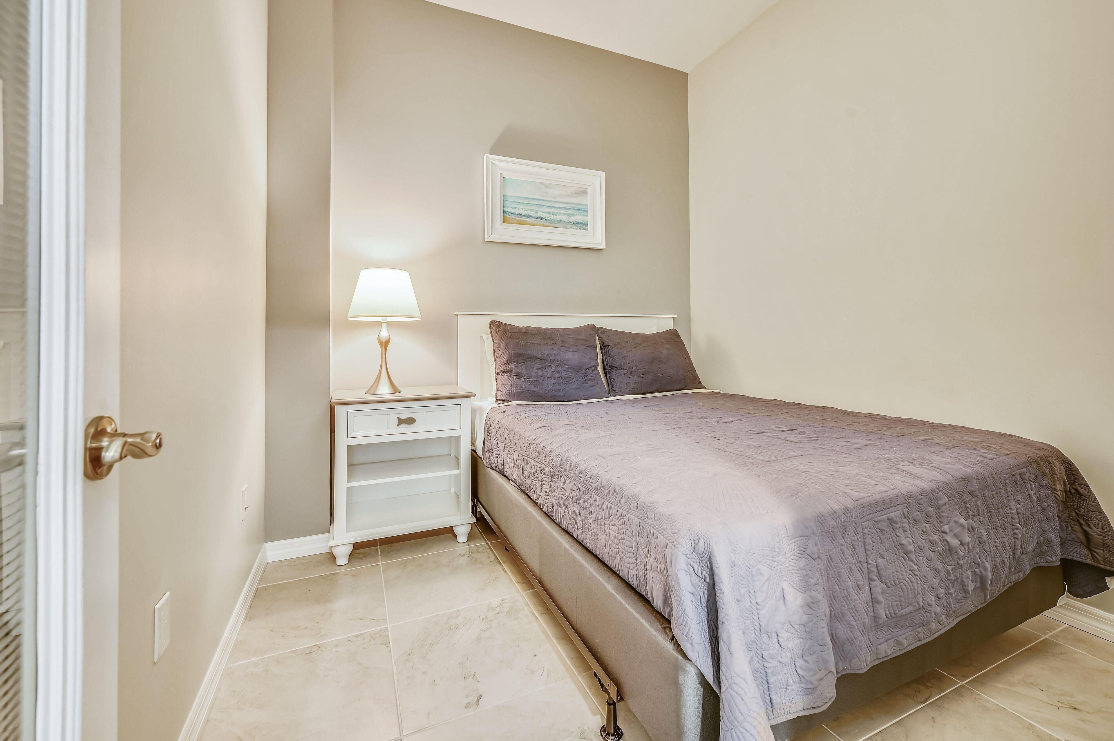A bedroom with a bed, nightstand, lamp, and a framed picture on the wall.