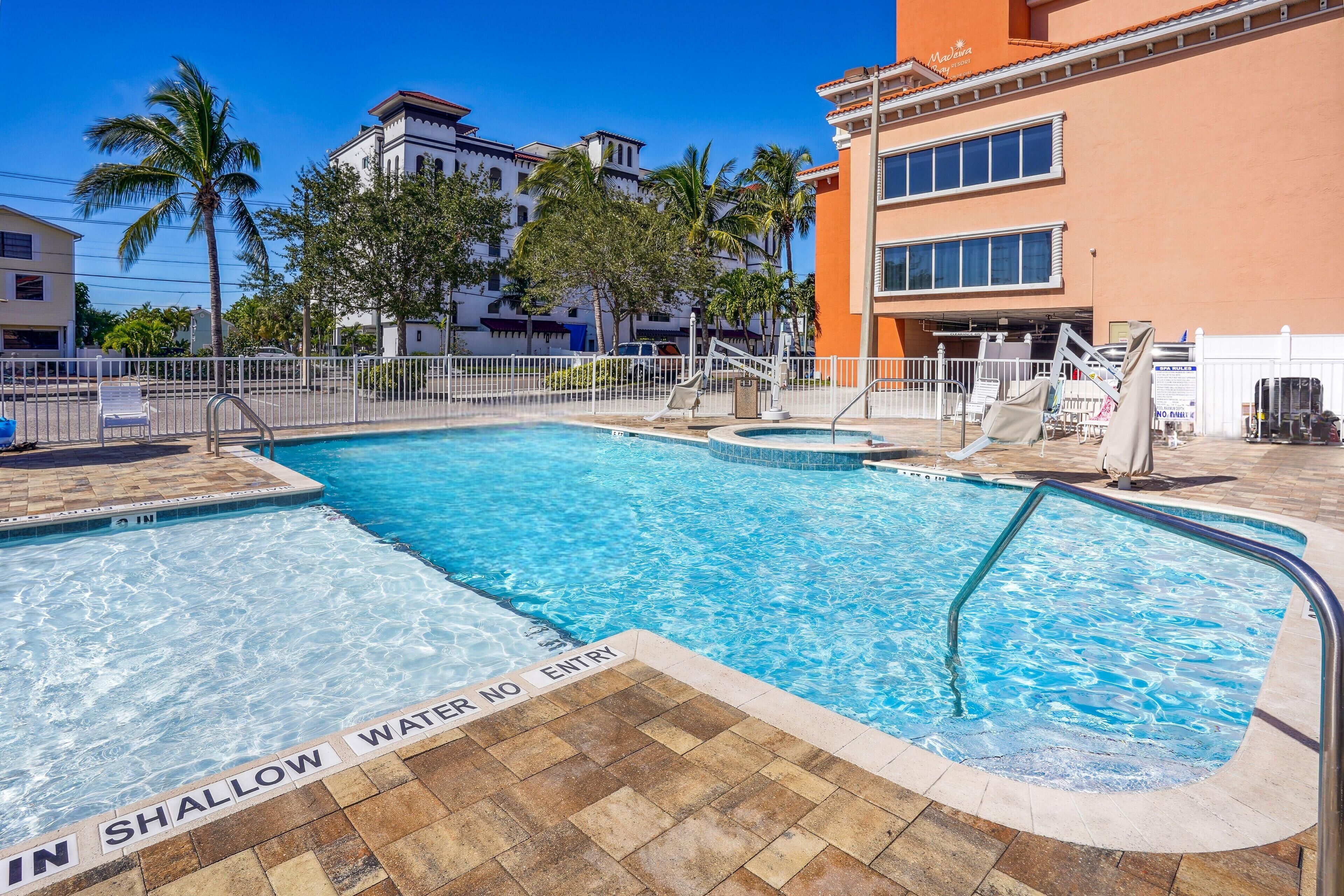 A swimming pool with a 'No Entry' sign, surrounded by a white fence and palm trees.