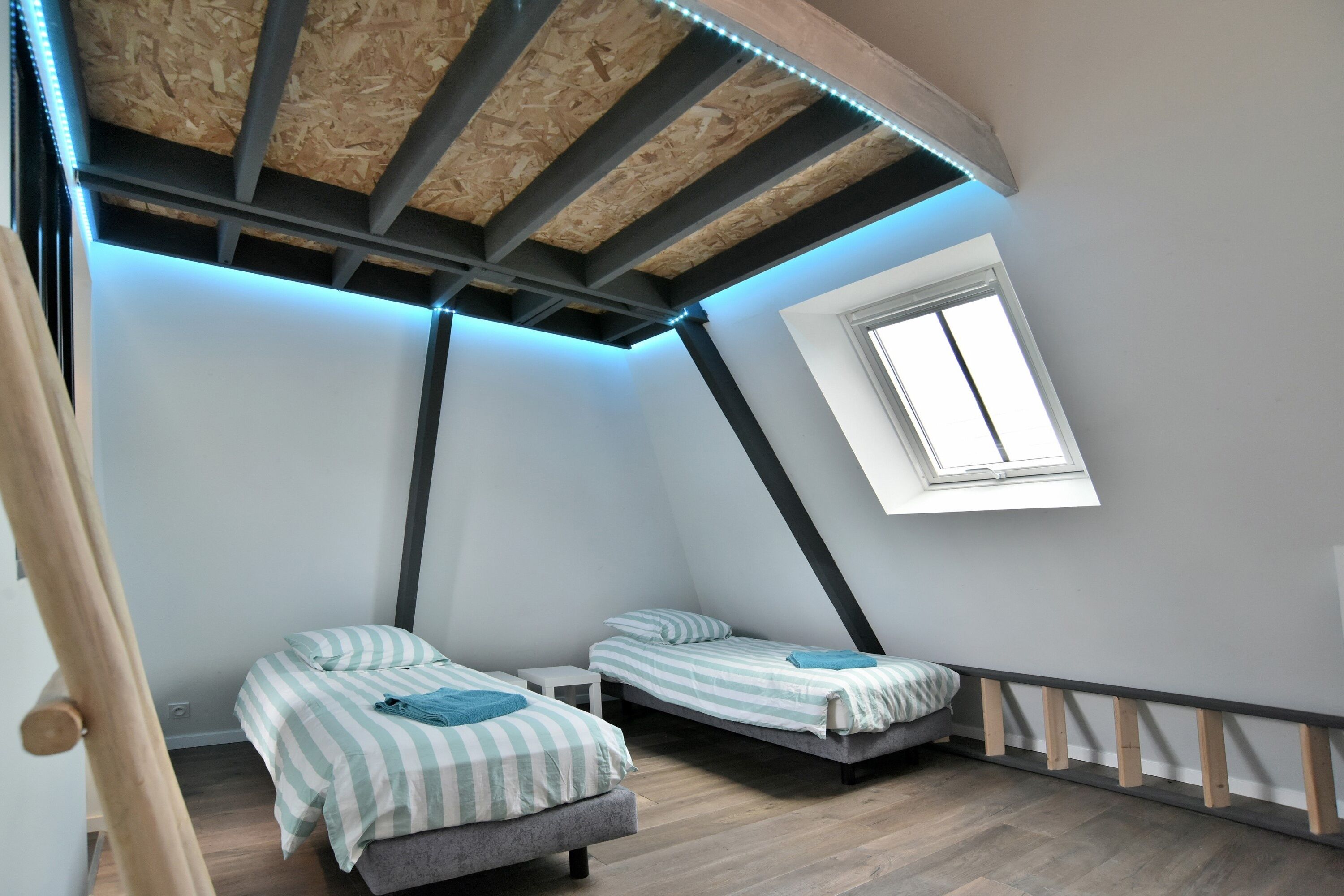 Un pequeño dormitorio abuhardillado triangular con dos camas, un tragaluz y vigas de madera a la vista.