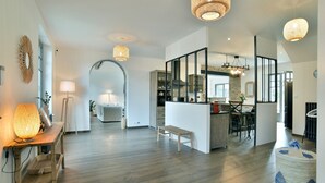 Amplia sala de estar con piso de madera, comedor con mesa y sillas, y área de cocina con mostrador y taburetes.