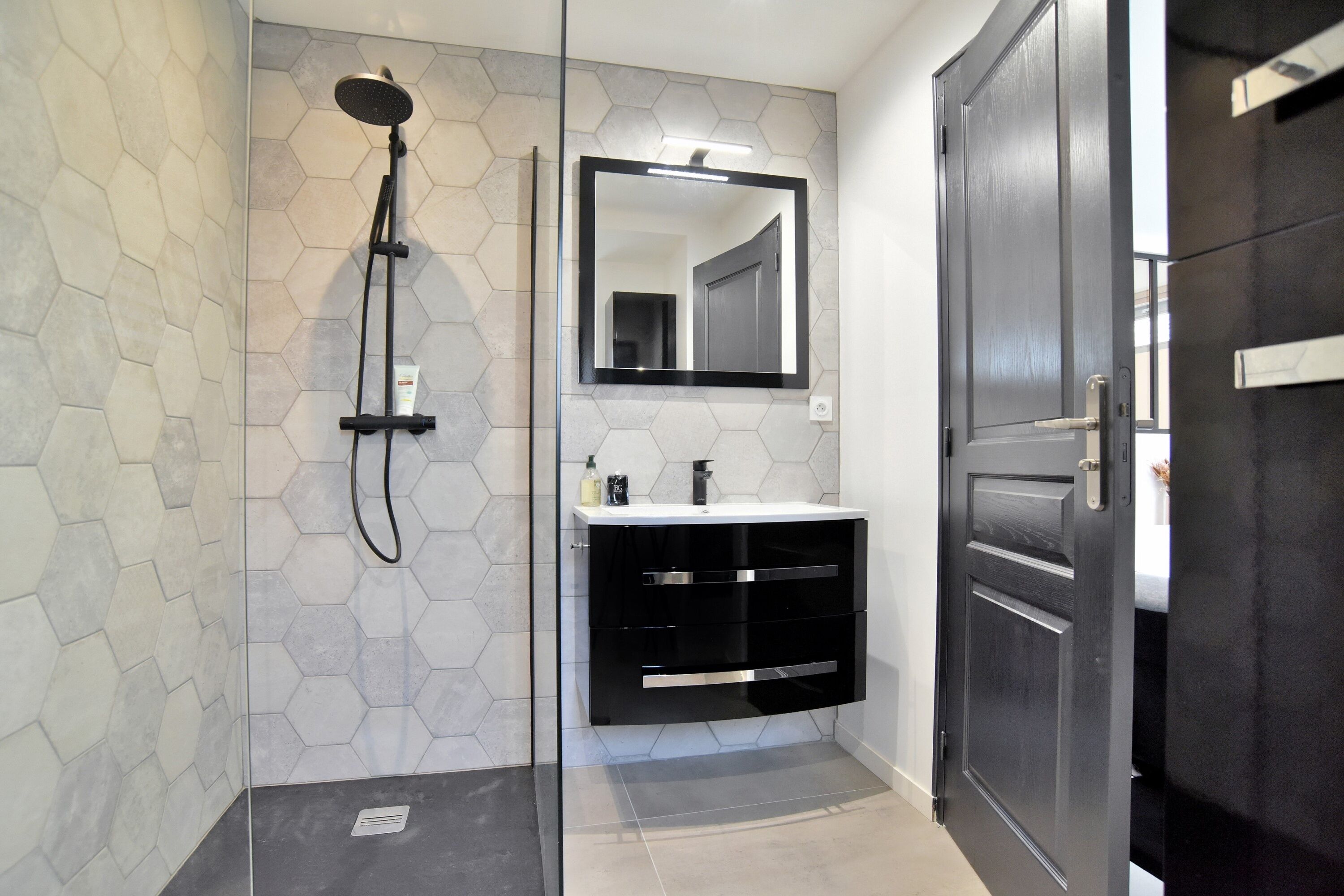 A modern bathroom with a hexagonal tile wall, a black vanity with a mirror, and a shower with a handheld showerhead.