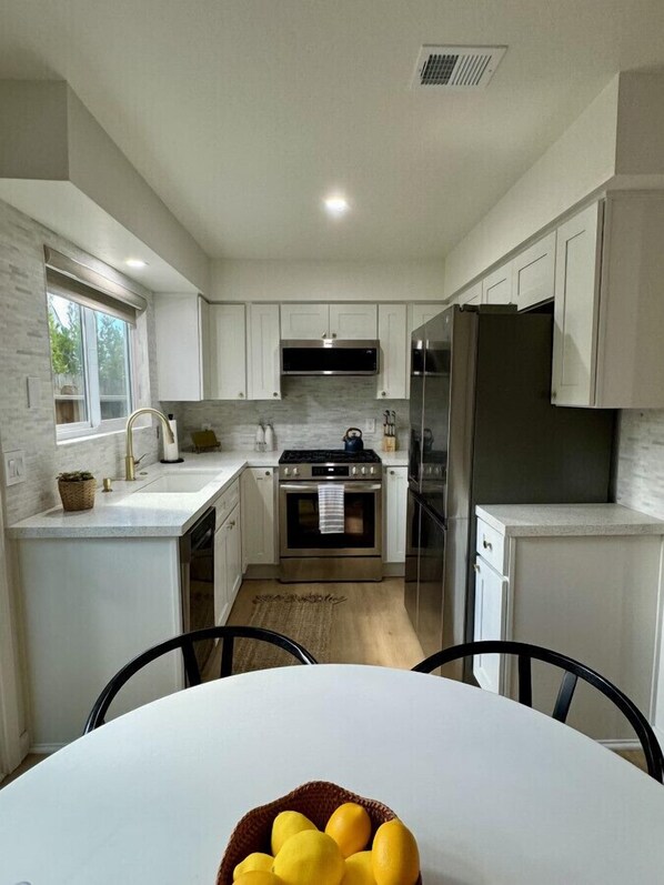 A modern kitchen with white cabinets, stainless steel appliances, and a dining area with a table and chairs.