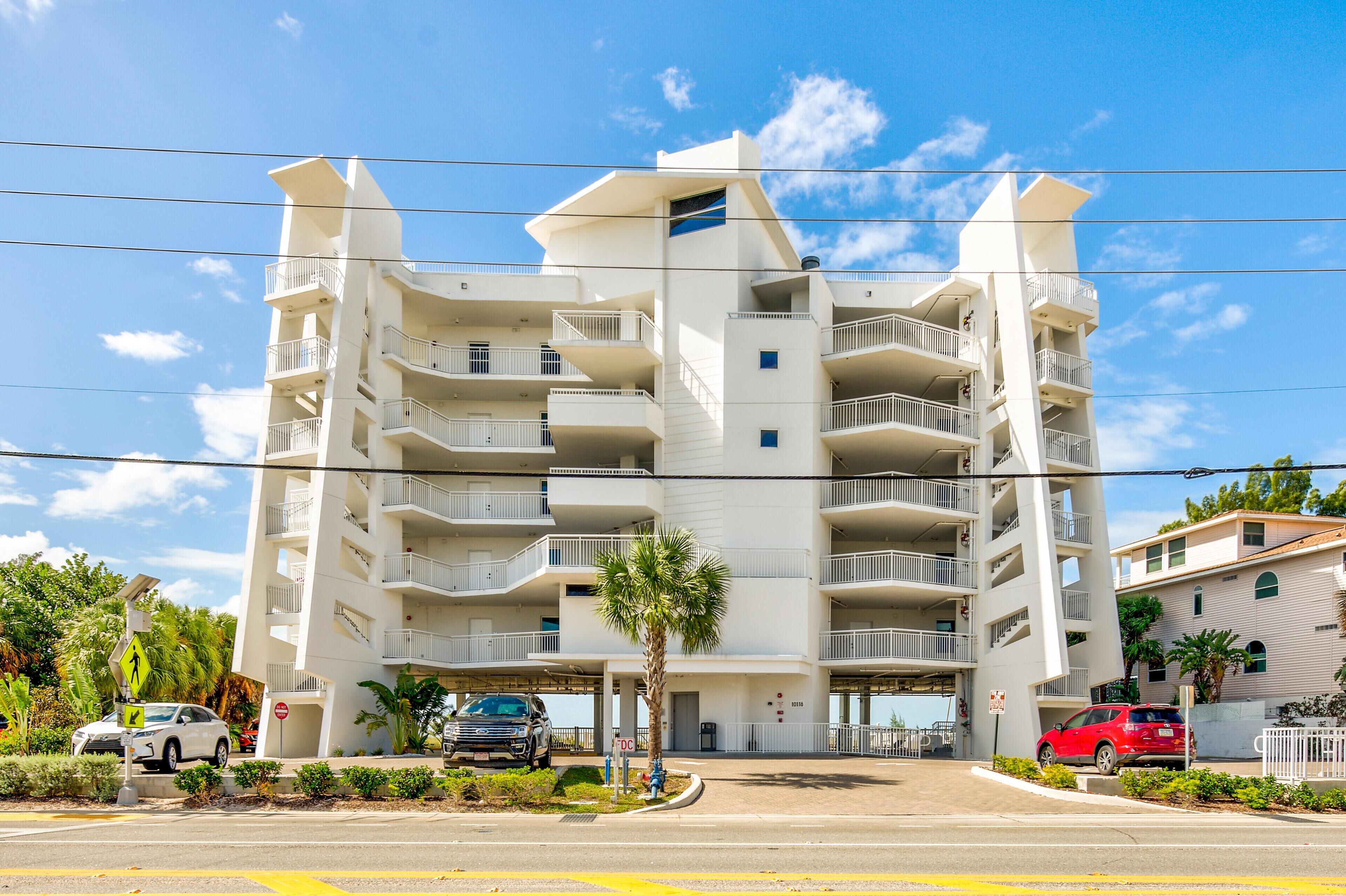 A multi-story residential building with balconies, a palm tree in front, and a clear blue sky.