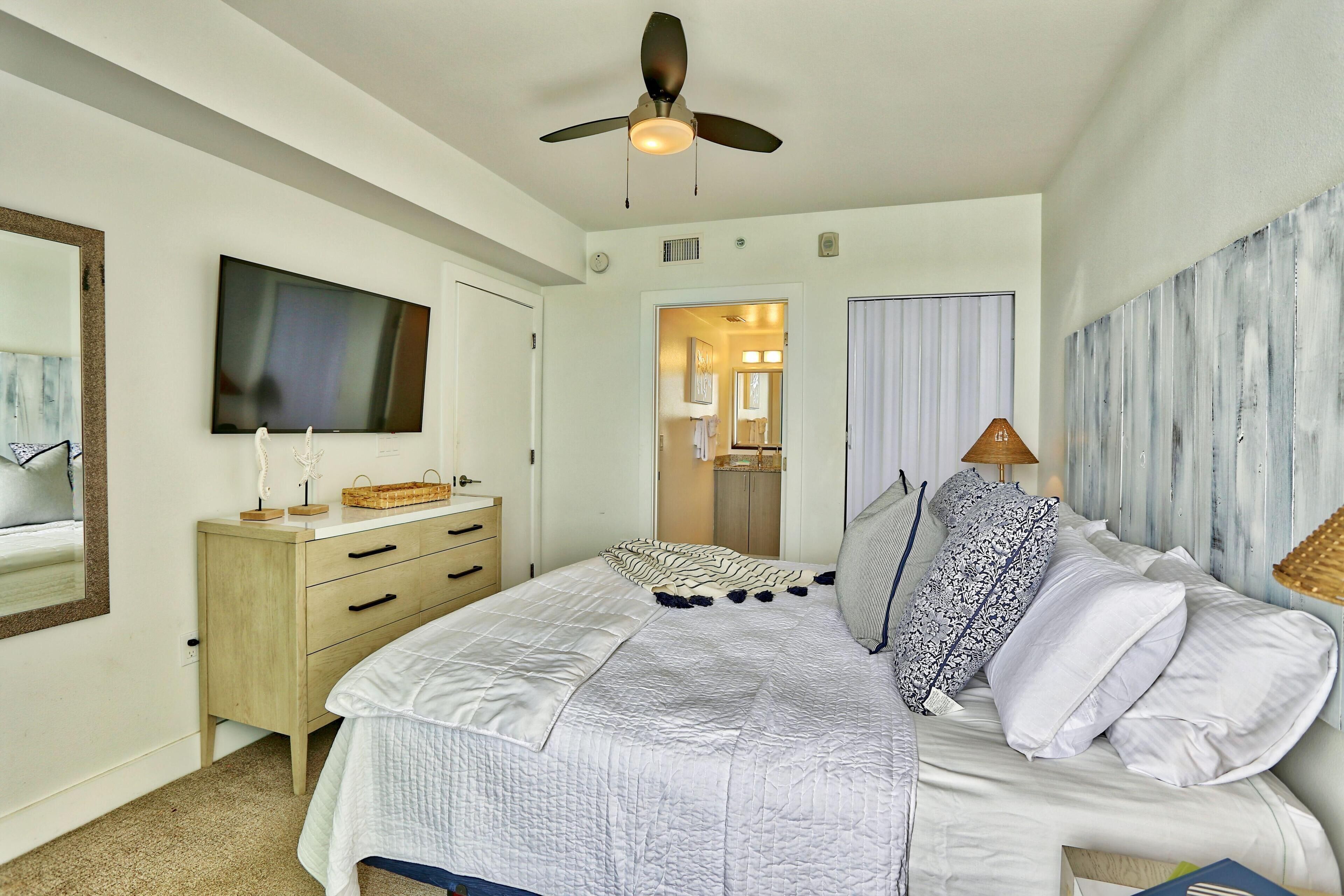 A bedroom with a bed, a ceiling fan, a TV, a dresser, and a mirror.