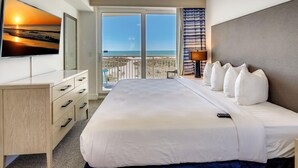 Ein Hotelzimmer mit Bett, Schreibtisch, Fernseher und einem Balkon mit Meerblick.