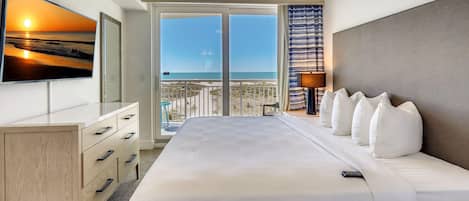 A hotel room with a bed, a desk, a TV, and a balcony with a view of the sea.