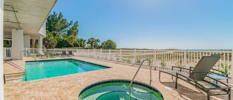 A swimming pool with a hot tub, lounge chairs, and a view of the ocean.