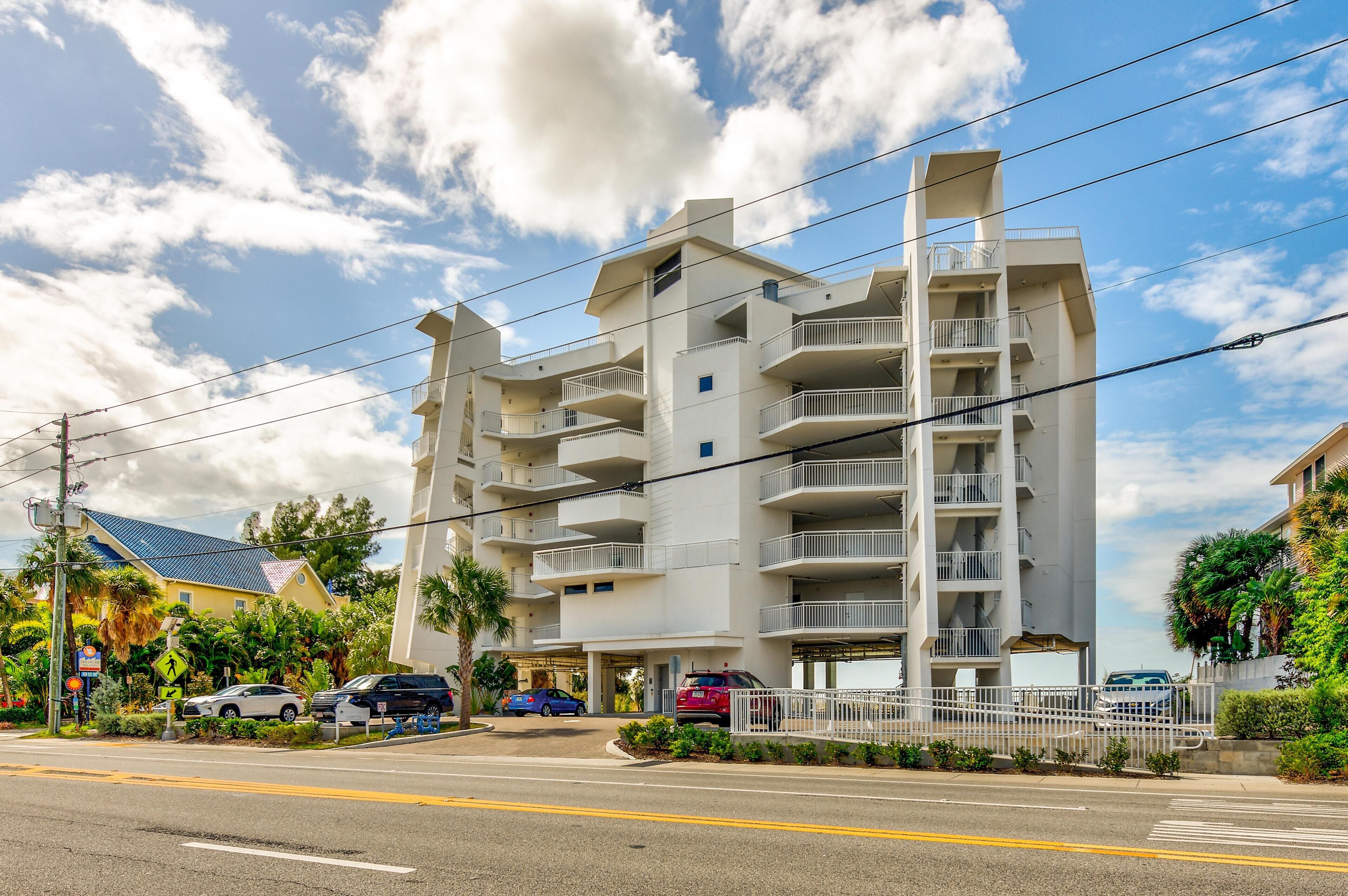 A multi-story residential building with balconies, a gated entrance, and a parking area.