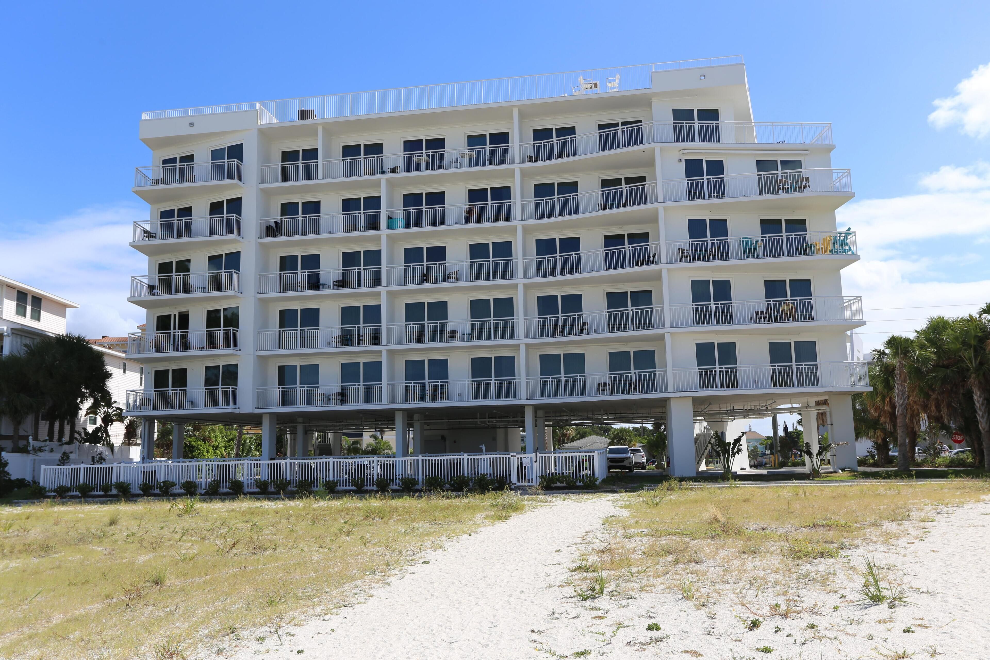 A multi-story hotel with balconies, a white exterior, and a sandy ground floor.